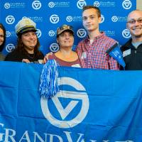 Five alumni pose for a photo while holding on to the GV flag